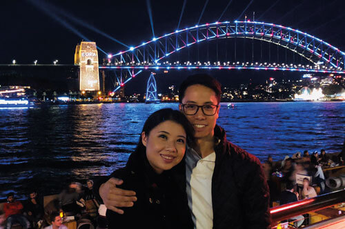 Photo showing Andrew and wife, Annie, with the Sydney Harbour Bridge during the Sydney Vivid light festival.